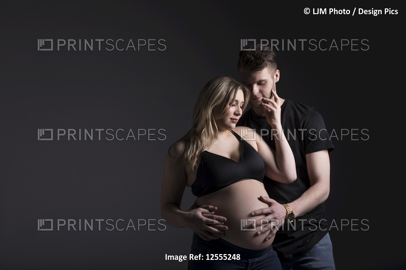 A young expectant couple looking down at their baby while the father is holding ...