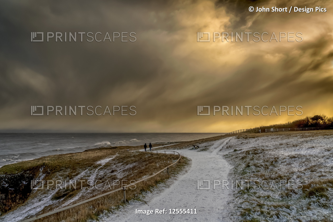 Two figures walking on the snowy path along the coast at dusk; South Shields, ...