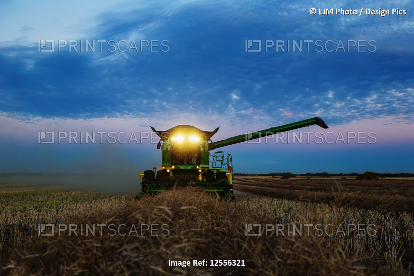 A fully loaded combine with its lights on arm out for transer, harvesting ...