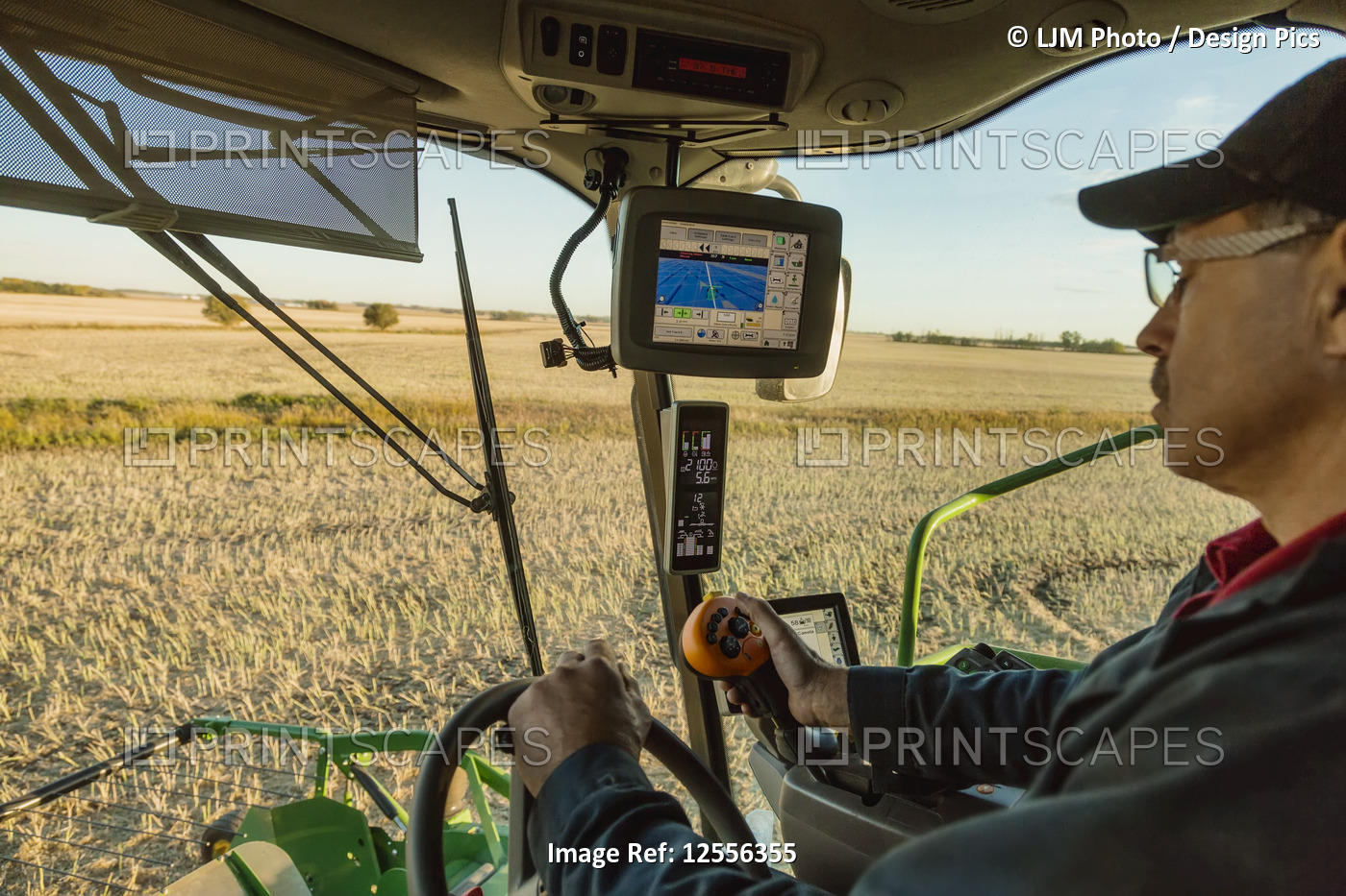 A farmer in the cab of his combine harvesting Canola at sunset and using ...