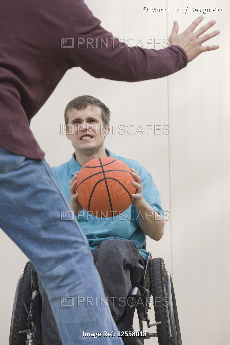 Young man sitting in a wheelchair and playing basketball with his father