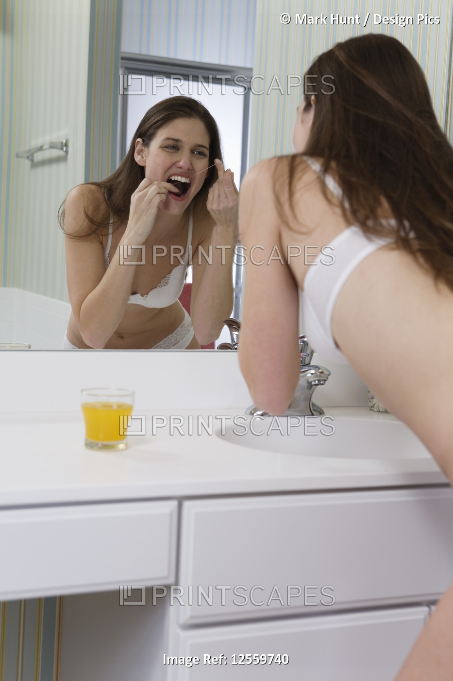 A young woman flossing her teeth in front of mirror.