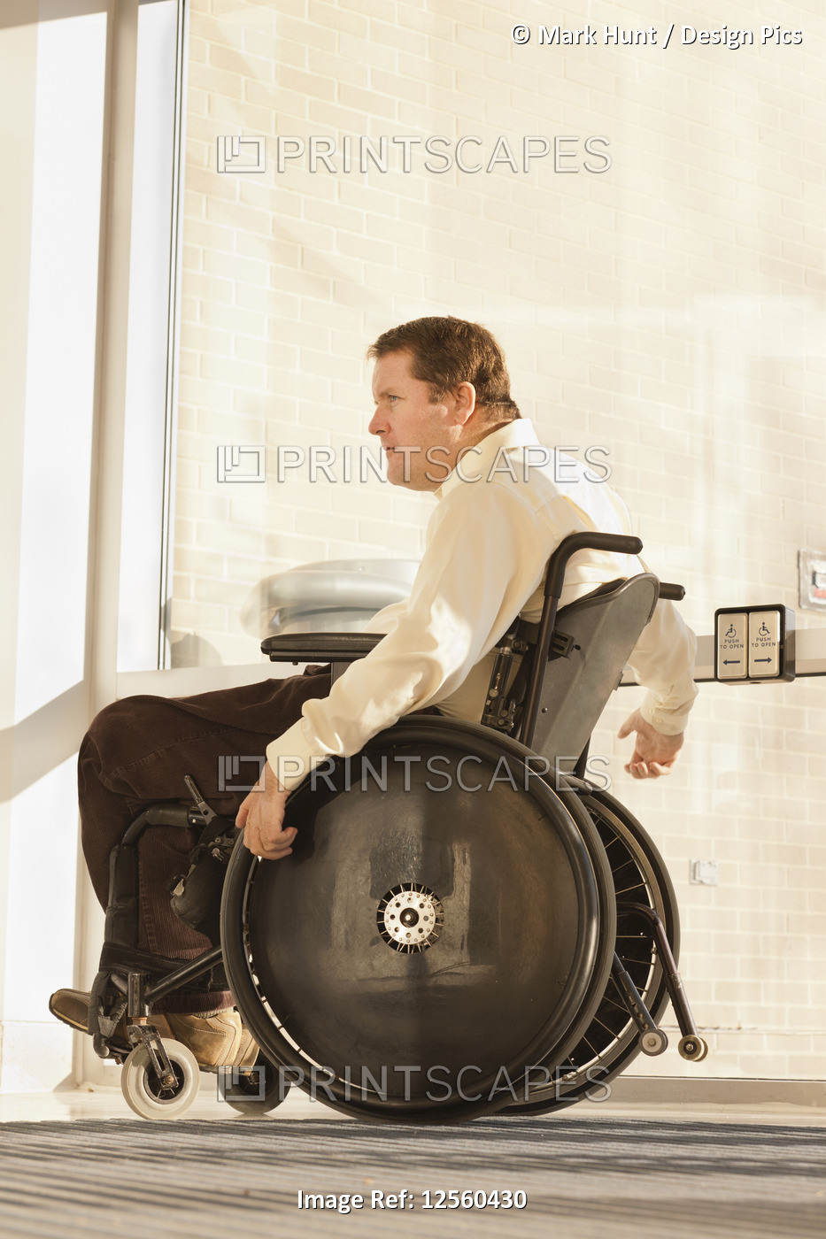 Businessman with spinal cord injury in wheelchair using automatic door opener ...
