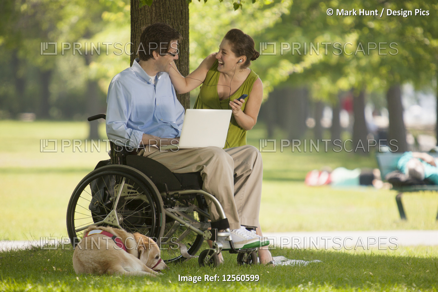 Man in wheelchair with pregnant wife enjoying electronics in a park