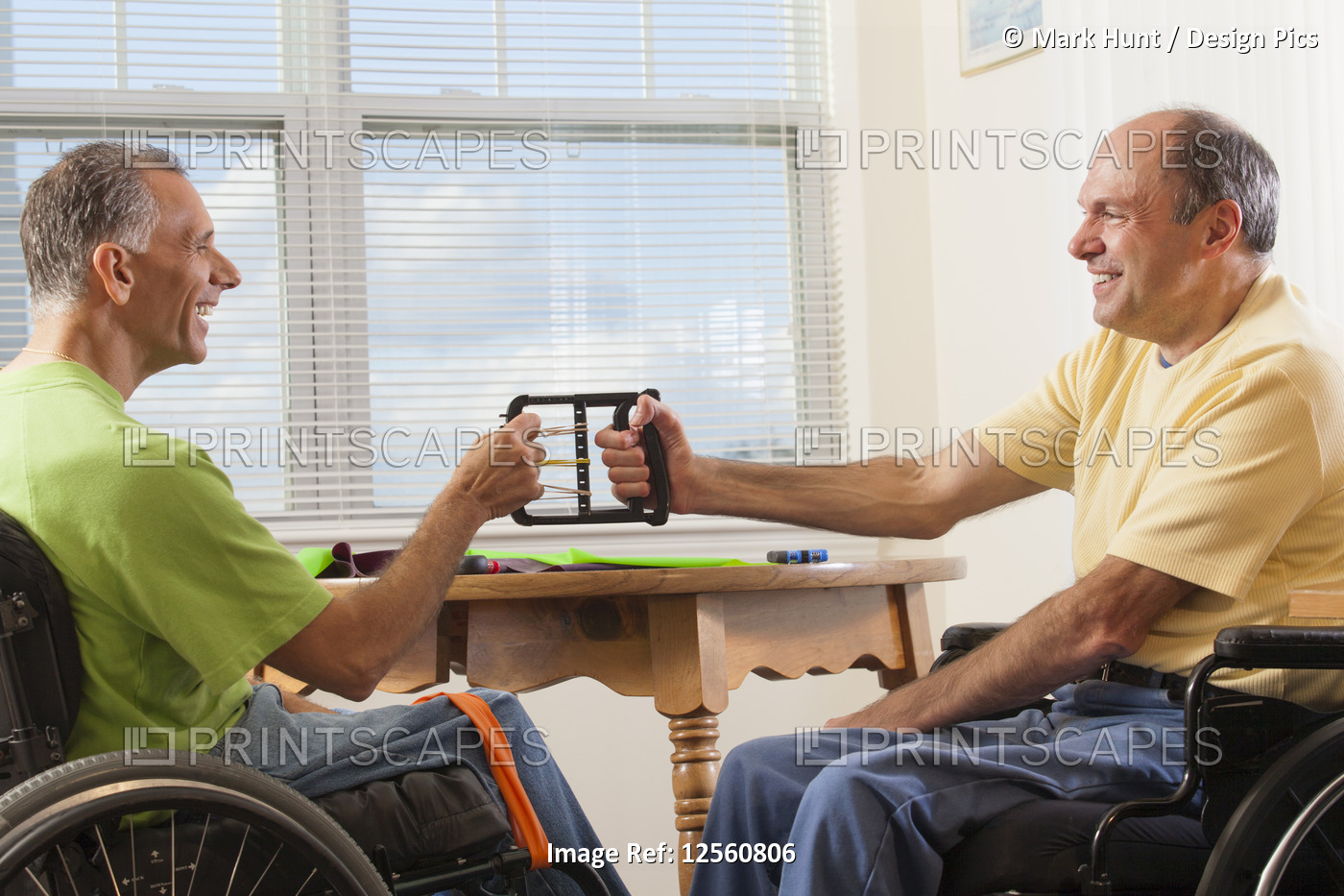 Two disabled men sitting in wheelchairs using hand strengthening equipment