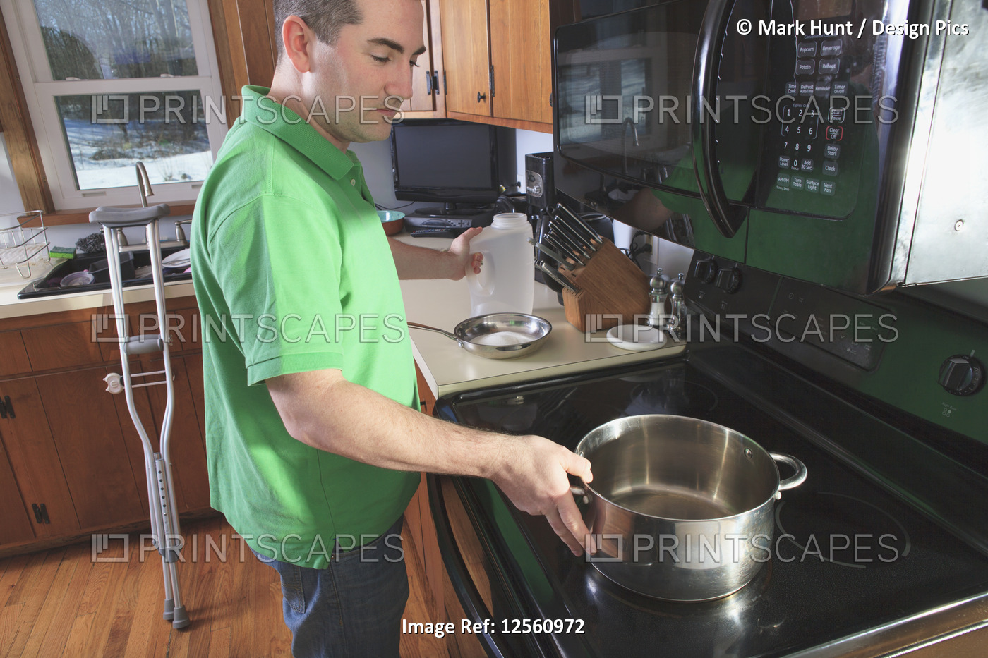Man after anterior cruciate ligament (ACL) surgery with crutches cooking in the ...