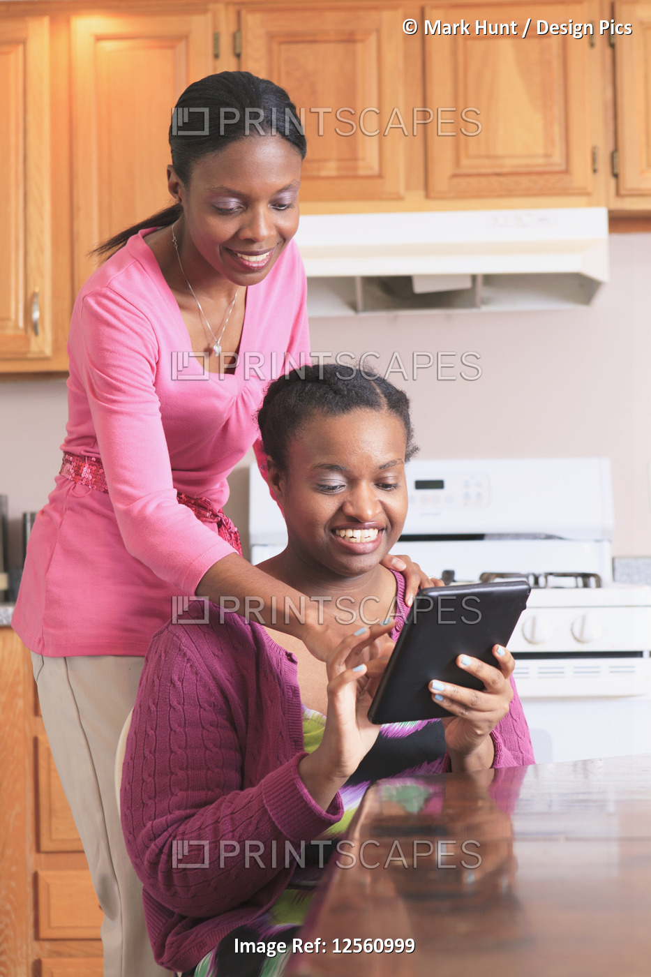 Two sisters looking at a digital tablet in the kitchen, one with learning ...