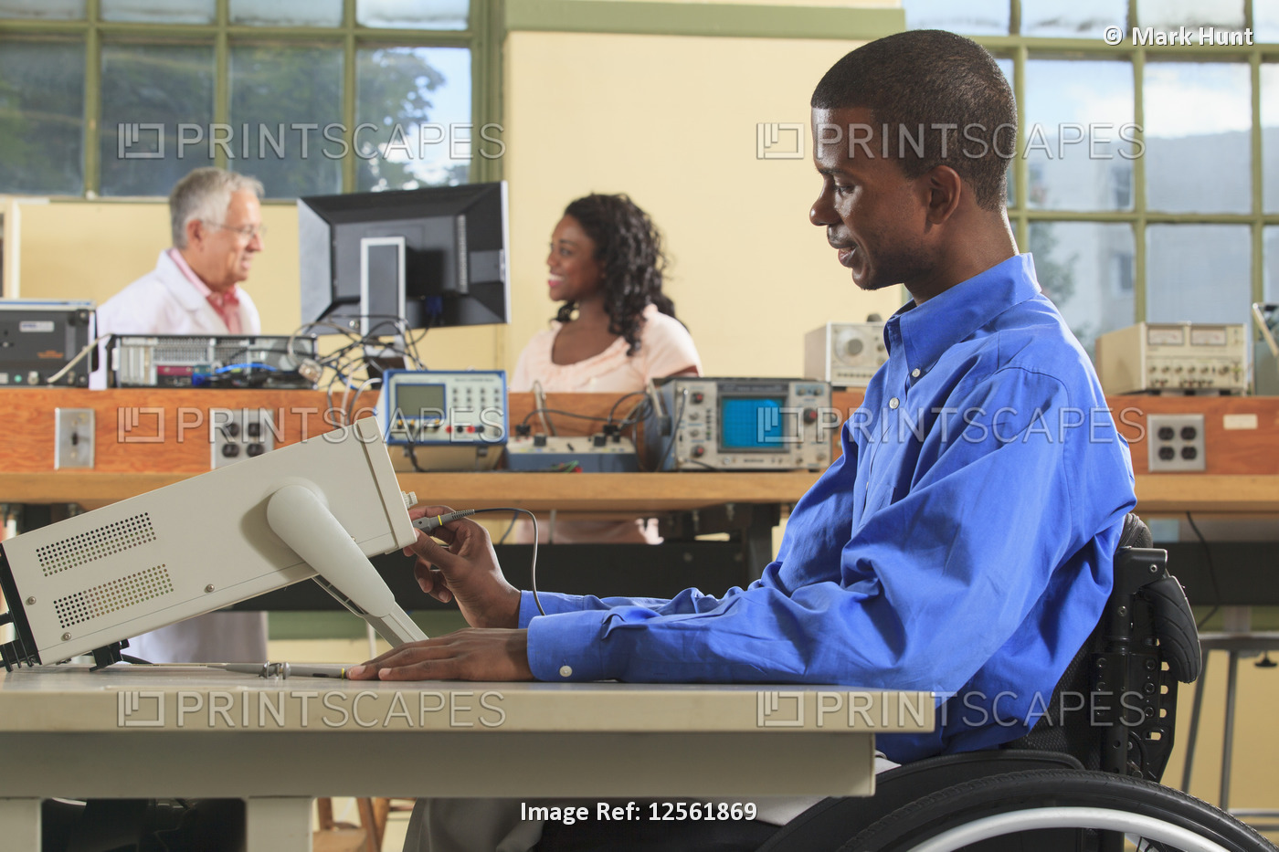 Engineering students in an electronics classroom, one in a wheelchair adjusting ...