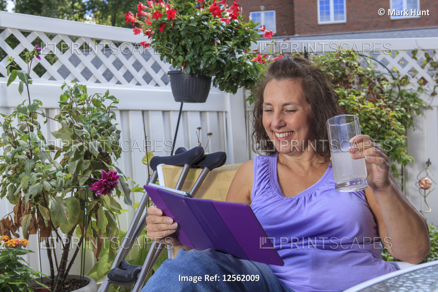 Woman with Spina Bifida on patio working on tablet and enjoying drink