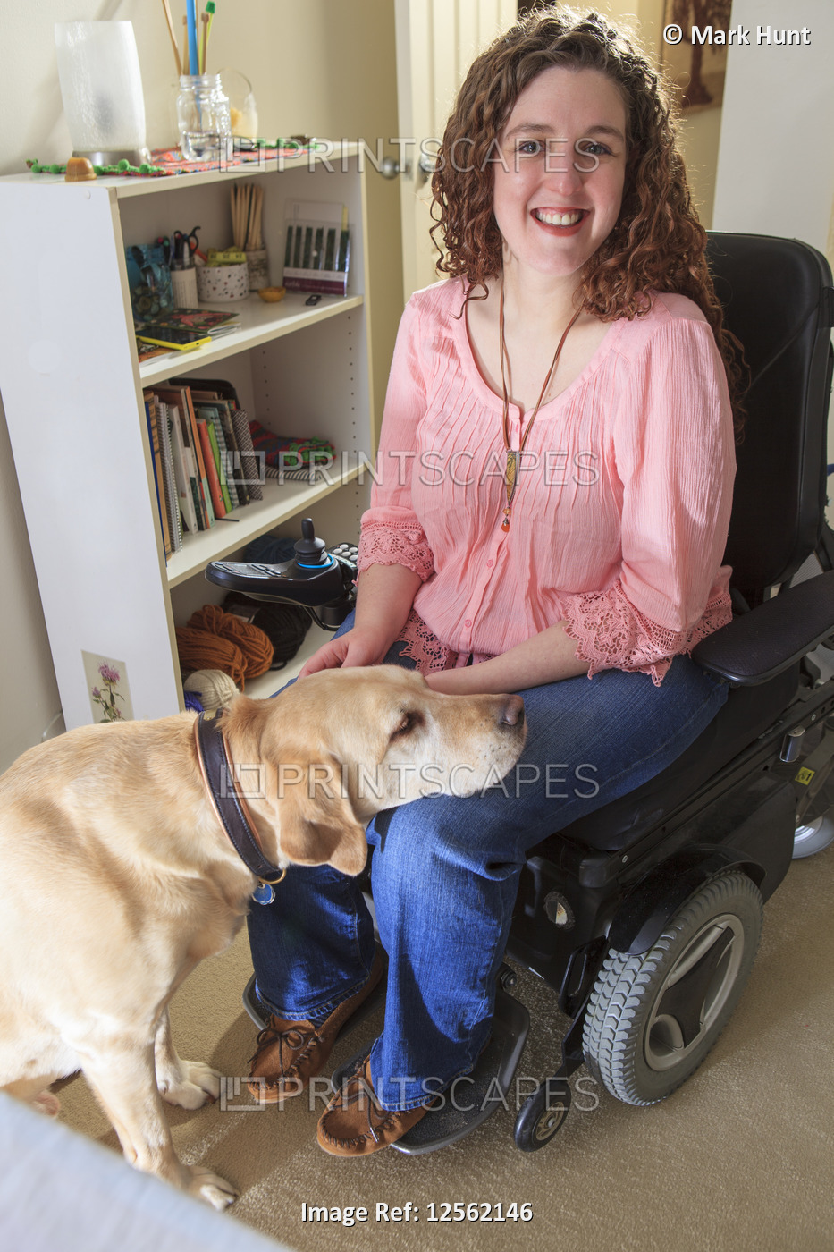 Woman with Muscular Dystrophy patting her service dog in her office