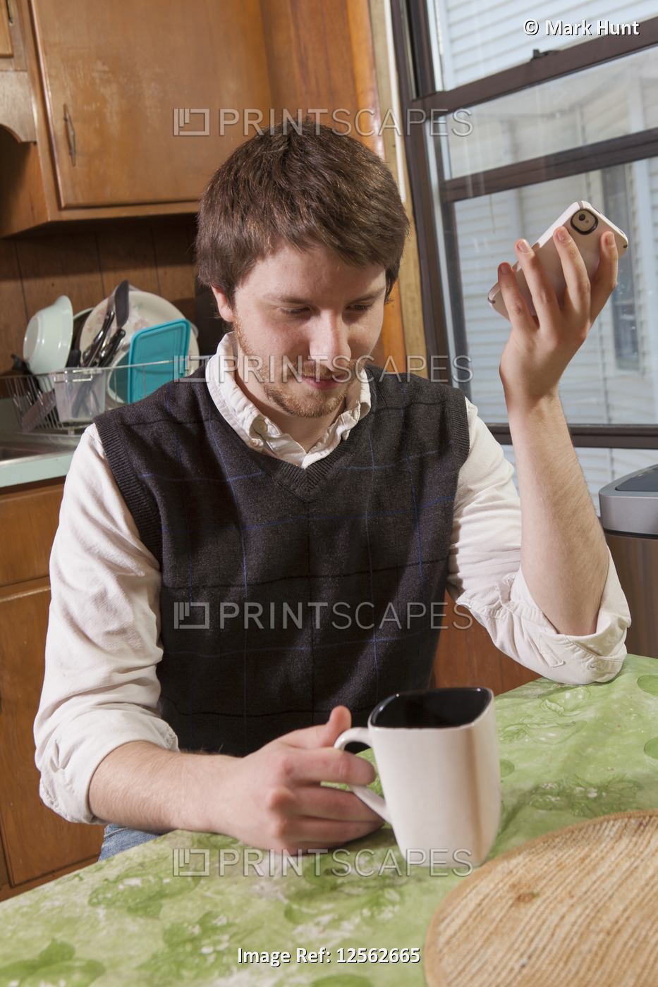 Blind man in his kitchen listening to assistive technology on his cell phone ...