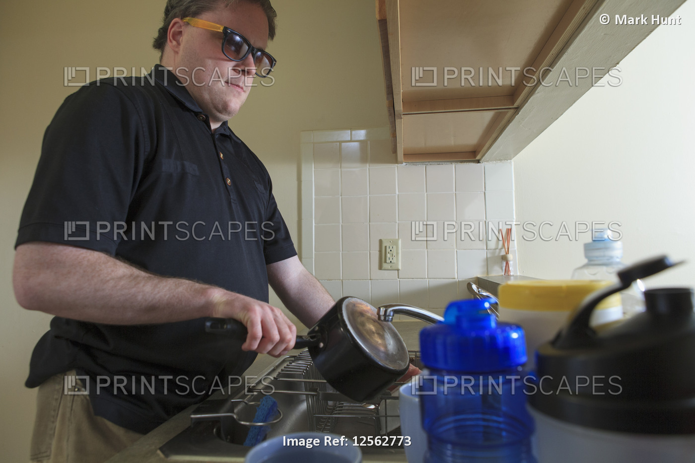 A man with a visual impairment stands at his kitchen sink washing dishes