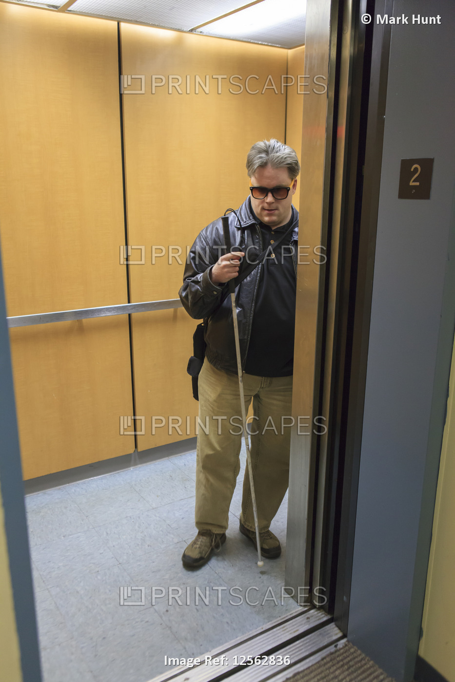 Man with visual impairment standing in a elevator with eyeglasses and a walking ...