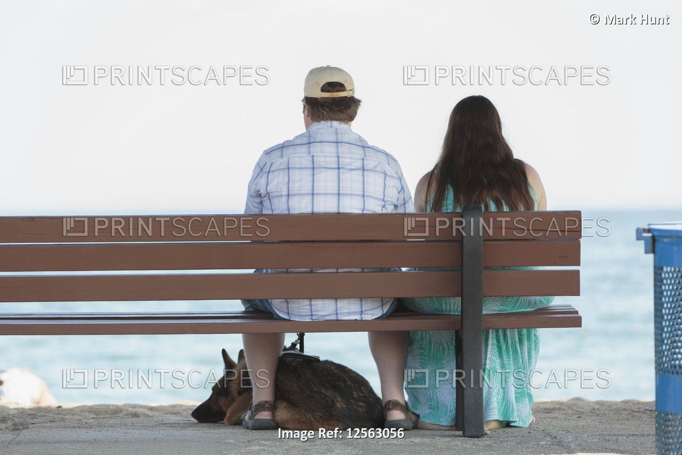 Blind couple sitting on a bench at the beach with their service dog