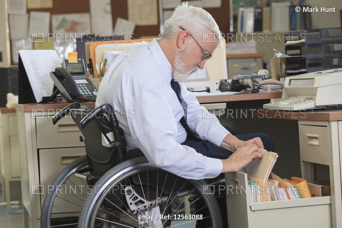 Man with Muscular Dystrophy in a wheelchair looking up paperwork in his office ...