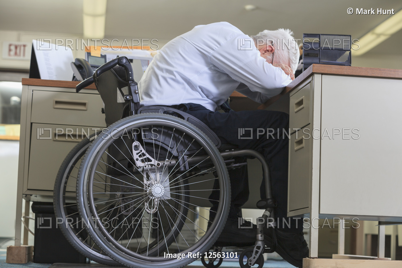 Man with Muscular Dystrophy in a wheelchair leaning down on his office desk