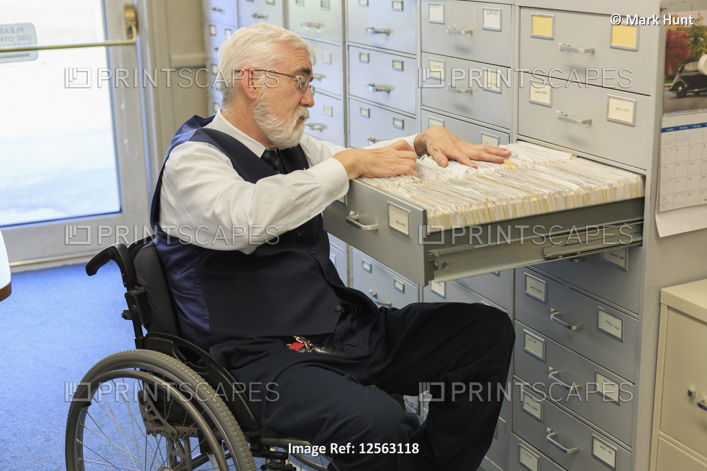 Man with Muscular Dystrophy in a wheelchair using a filing system in his office