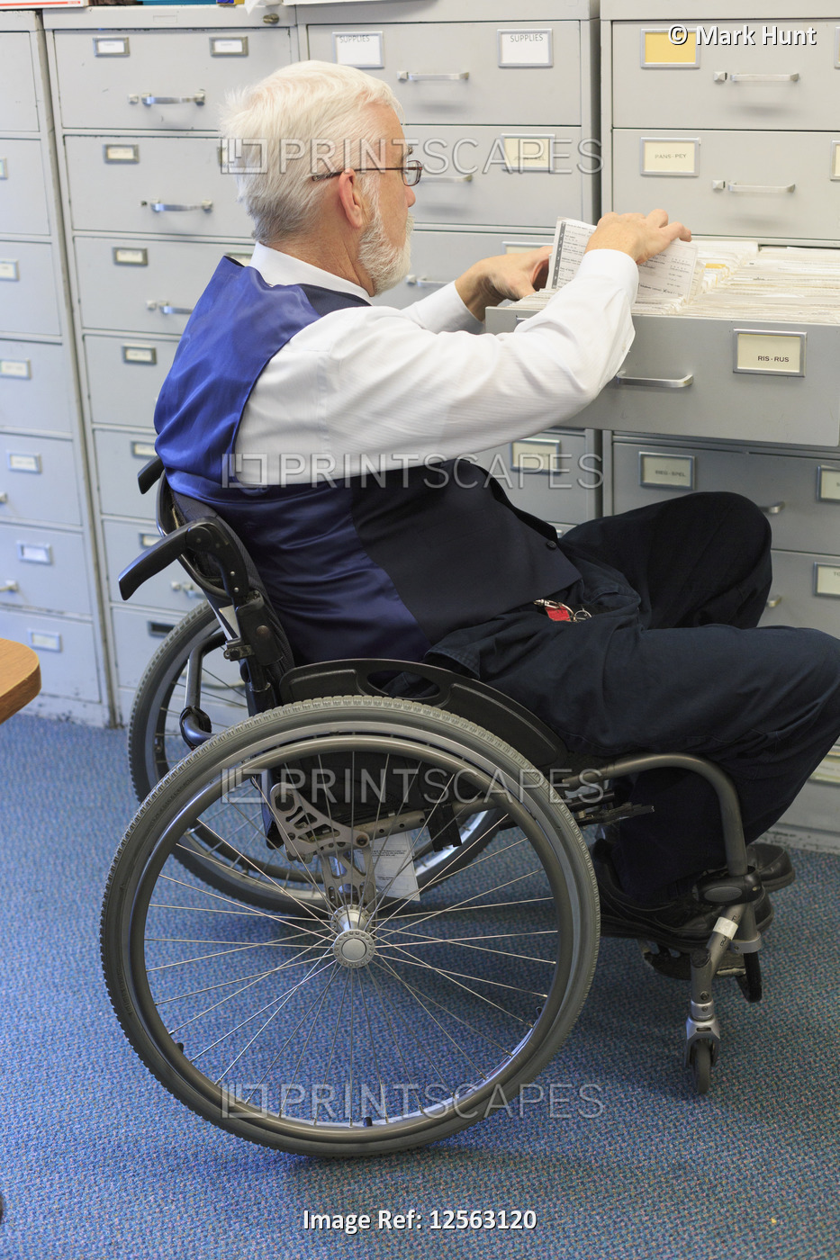 Man with Muscular Dystrophy in a wheelchair pulling documents in an office