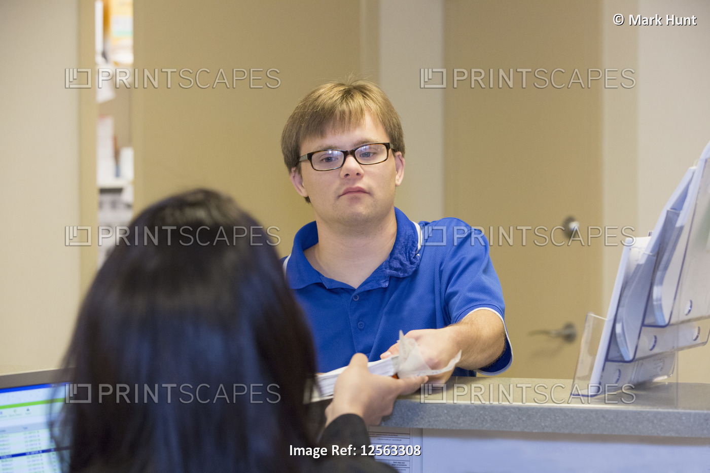 Young man with Down Syndrome giving out paperwork to his colleague in a health ...