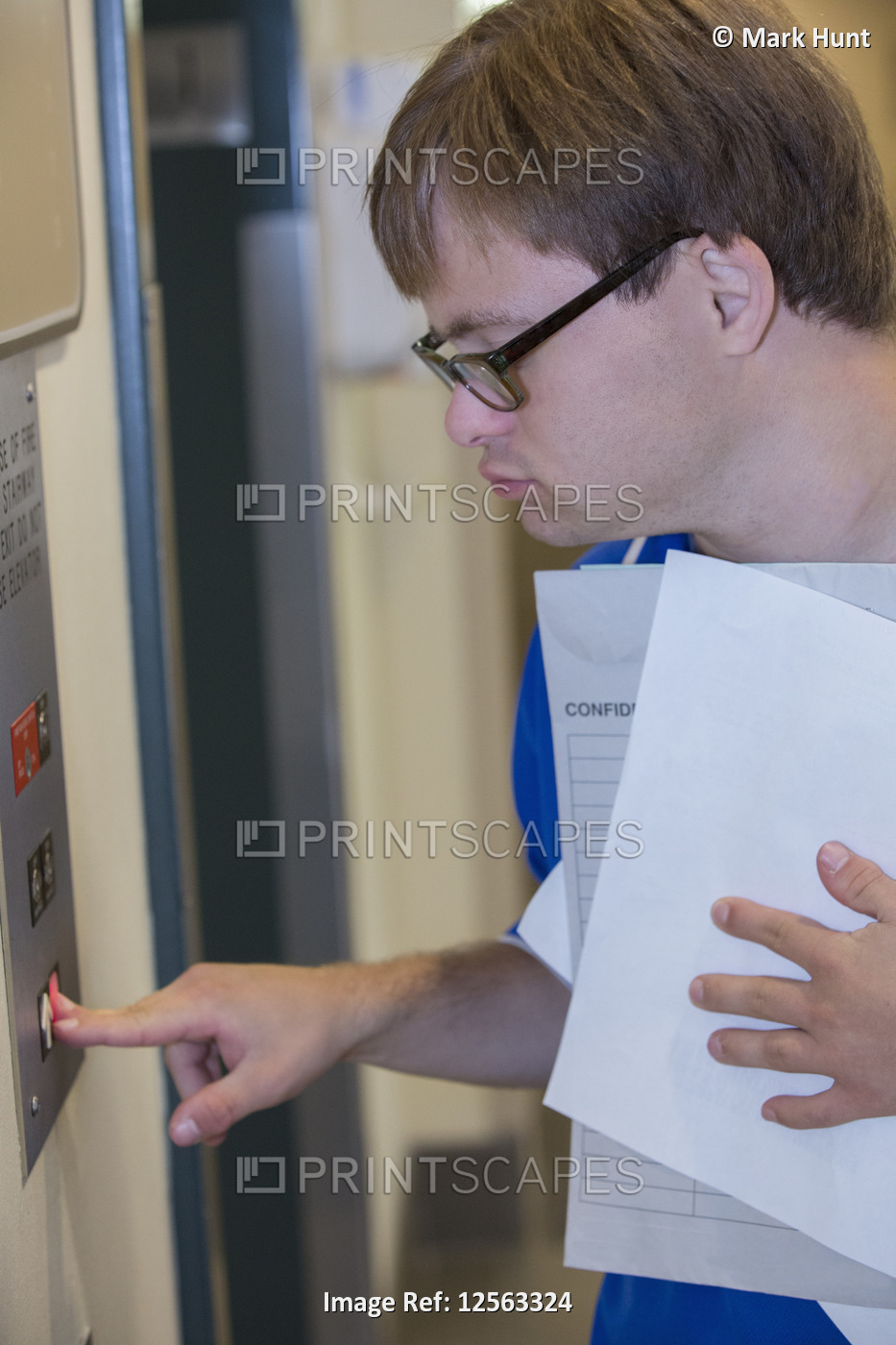 Young man with Down Syndrome using the elevator while delivering paperwork in a ...