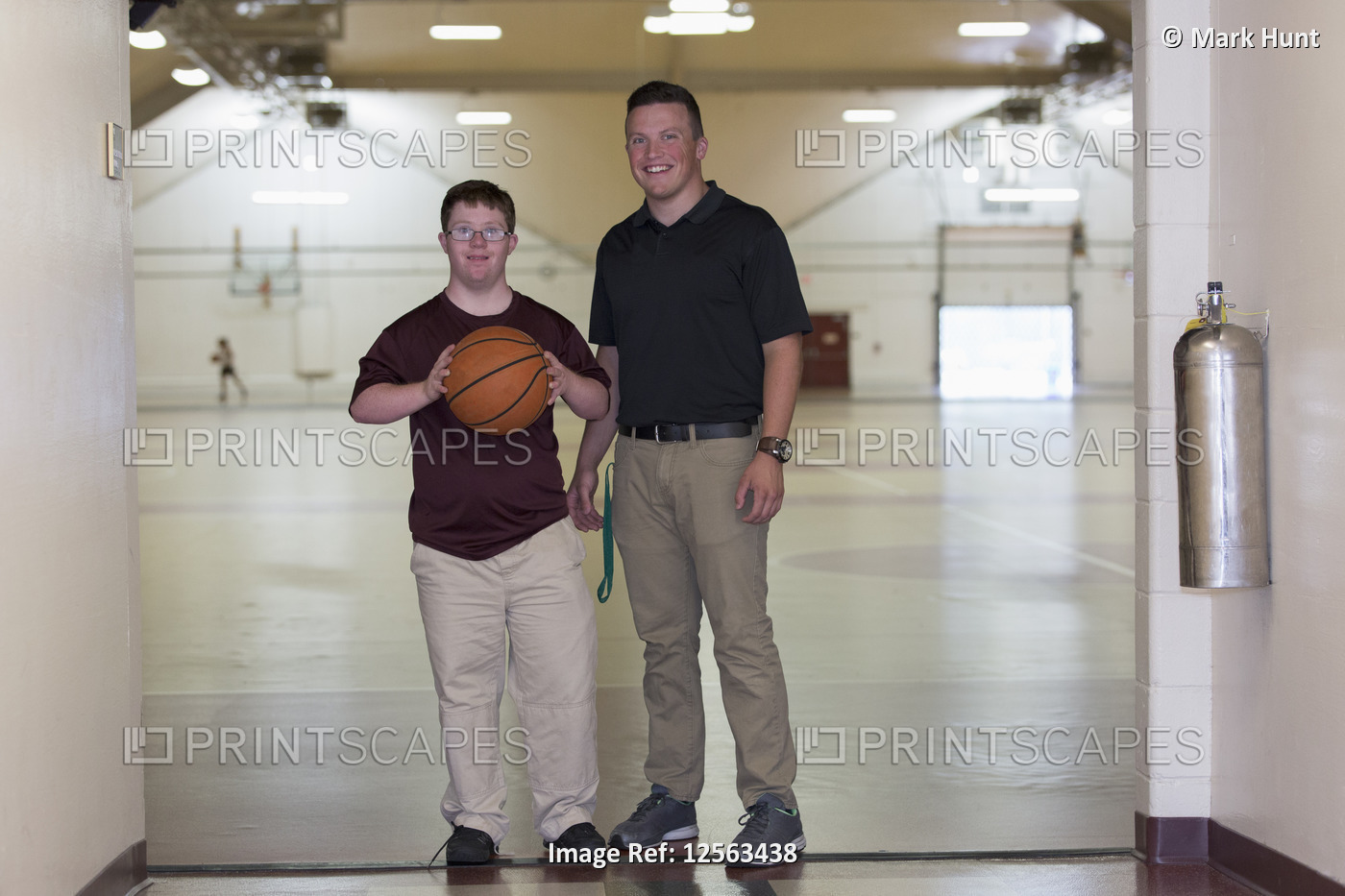 Young man with Down Syndrome playing basketball in school gym with his friend