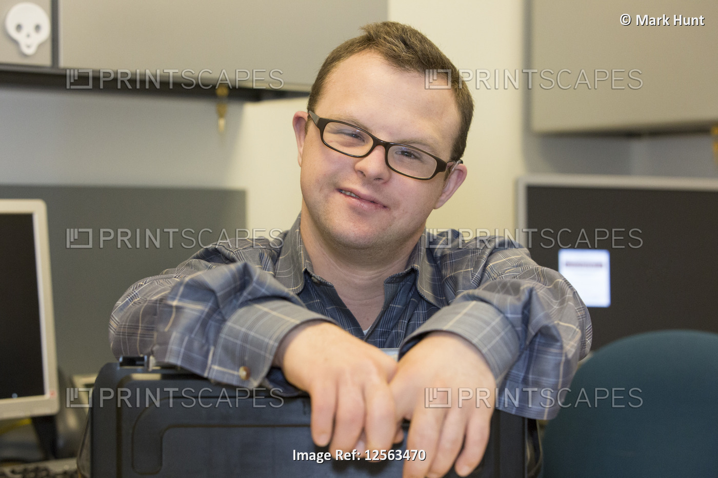 Portrait of happy hospital aid worker with Down Syndrome sitting at his desk in ...