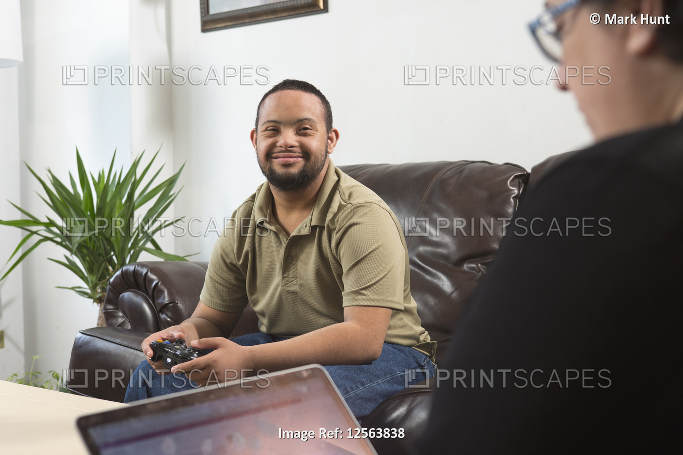 Happy African American man with Down Syndrome using a game controller with his ...