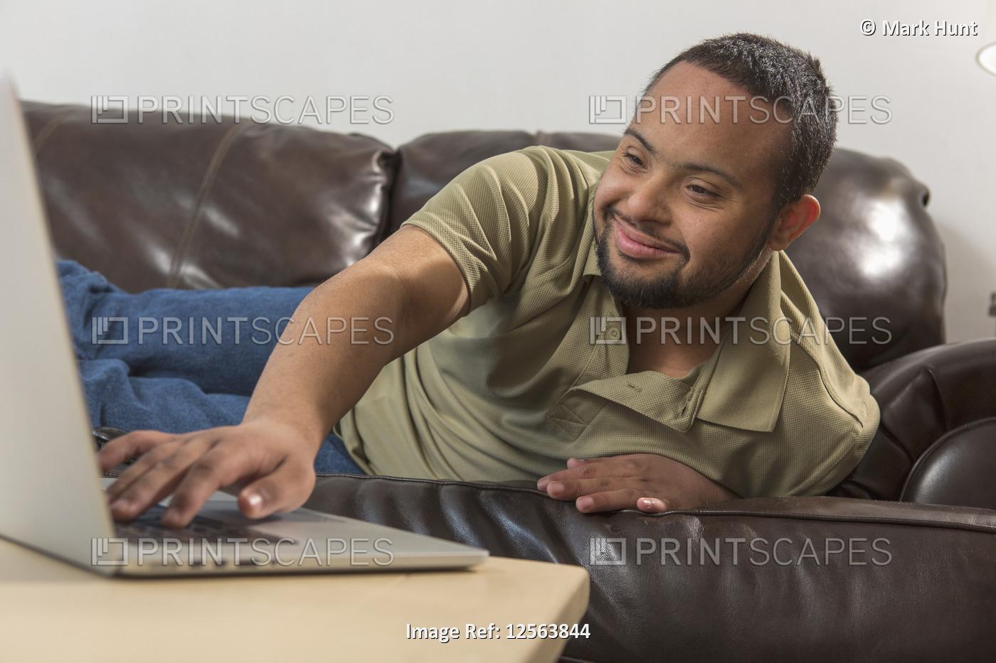 Happy African American man with Down Syndrome using a laptop from his sofa at ...
