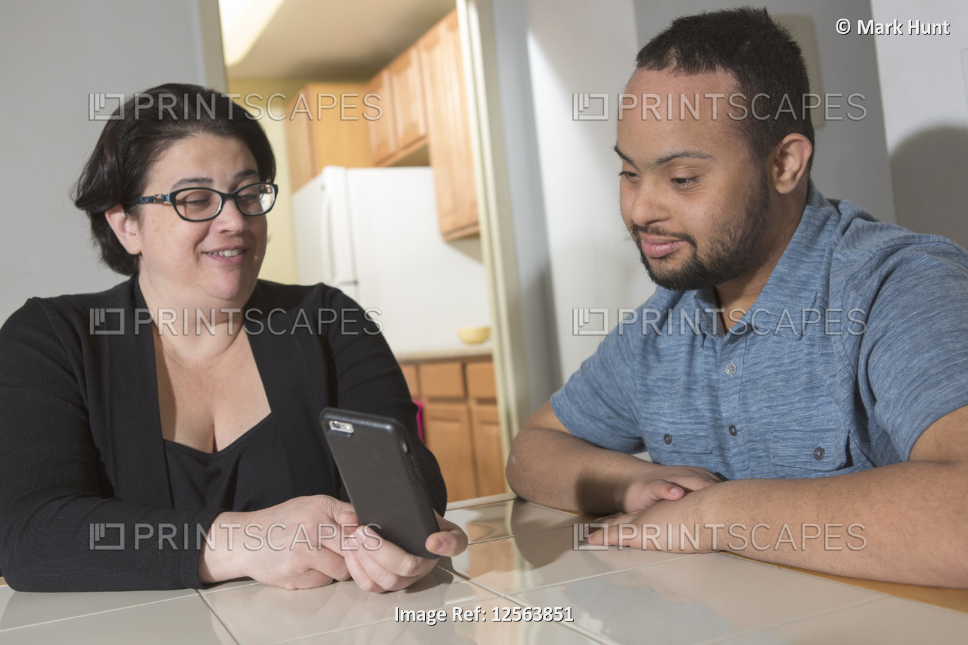 African American man with Down Syndrome using a cell phone with his mother at ...