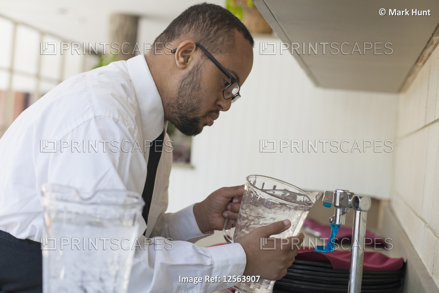 African American man with Down Syndrome as a waiter filling jug of water in ...