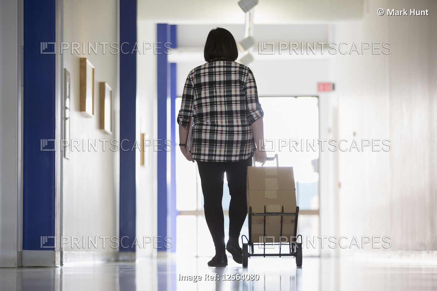 Asian woman with a Learning Disability taking boxes down an office hallway