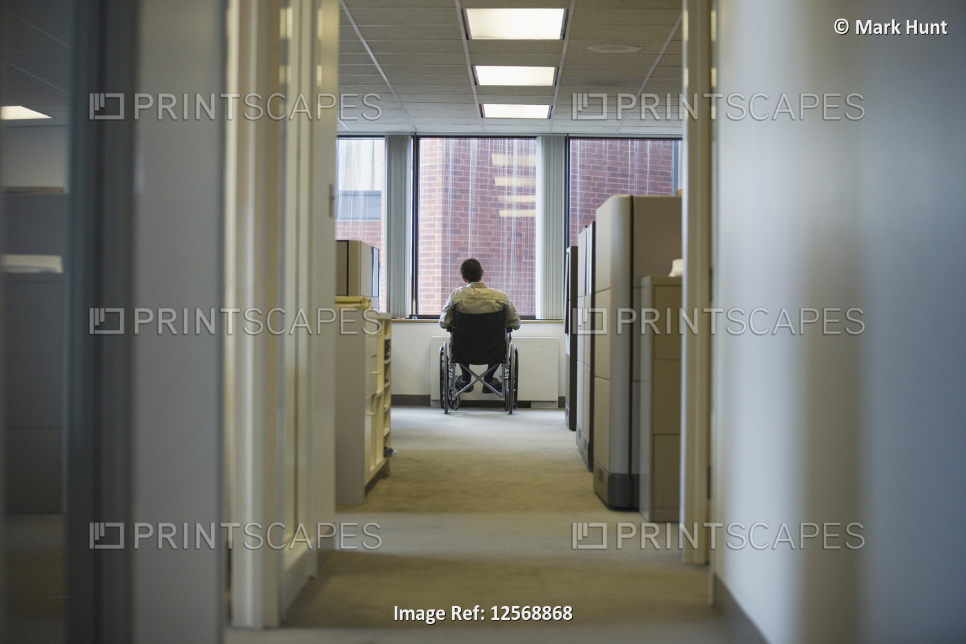 Rear view of a man sitting in a wheelchair in an office