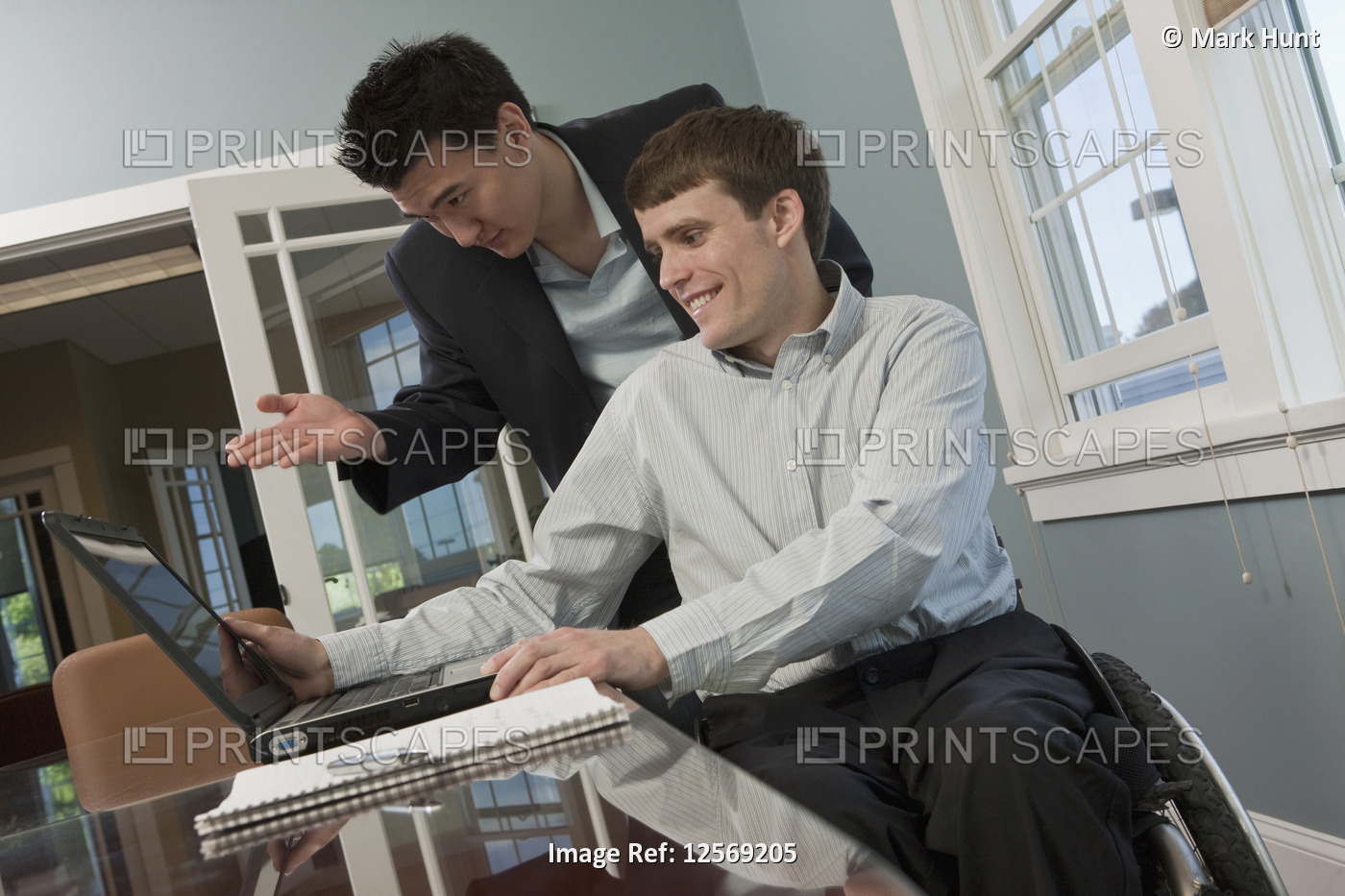 Businessman with spinal cord injury using a laptop with his colleague in an ...