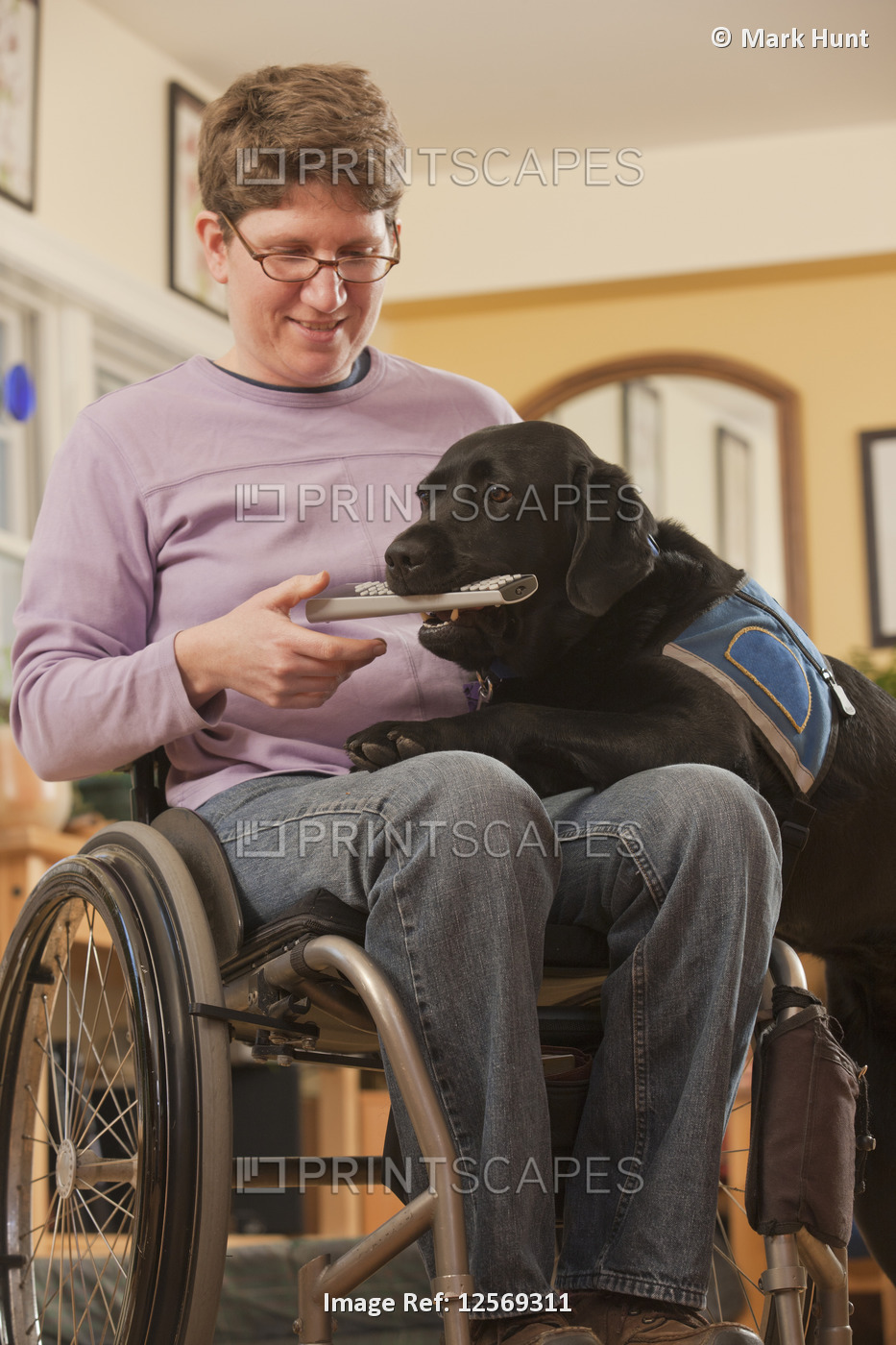 A service dog brings a remote control to a woman in a wheelchair in her home