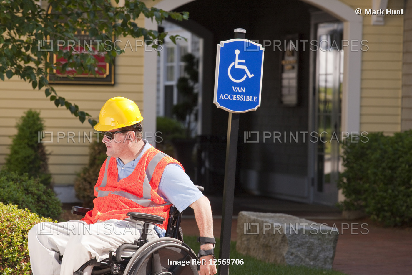 Man in wheelchair with hard hat and reflective vest going by a sign for ...