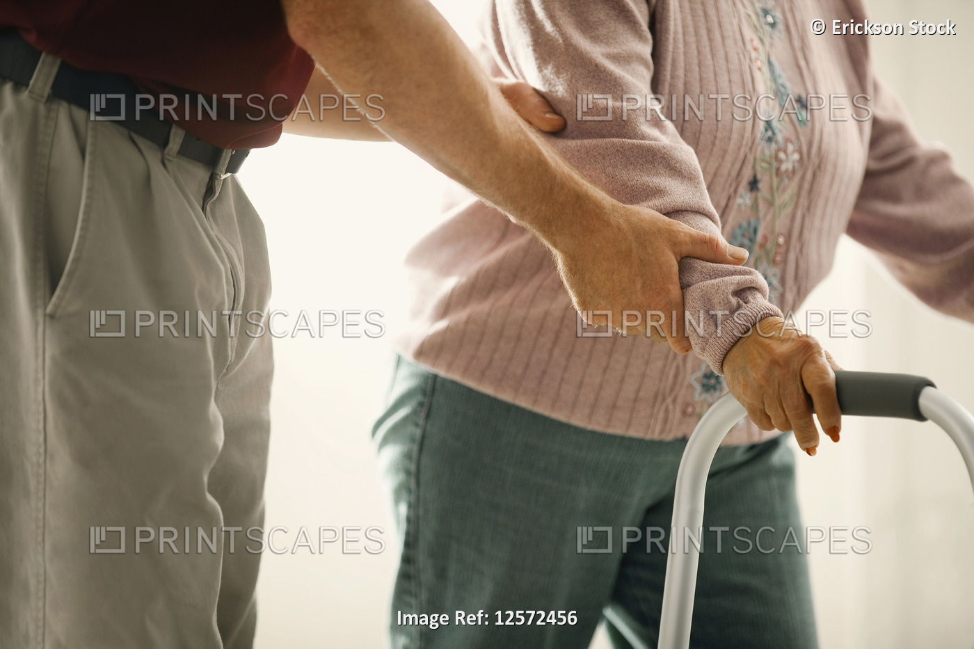 Hands of a male nurse supporting an elderly woman using a walker