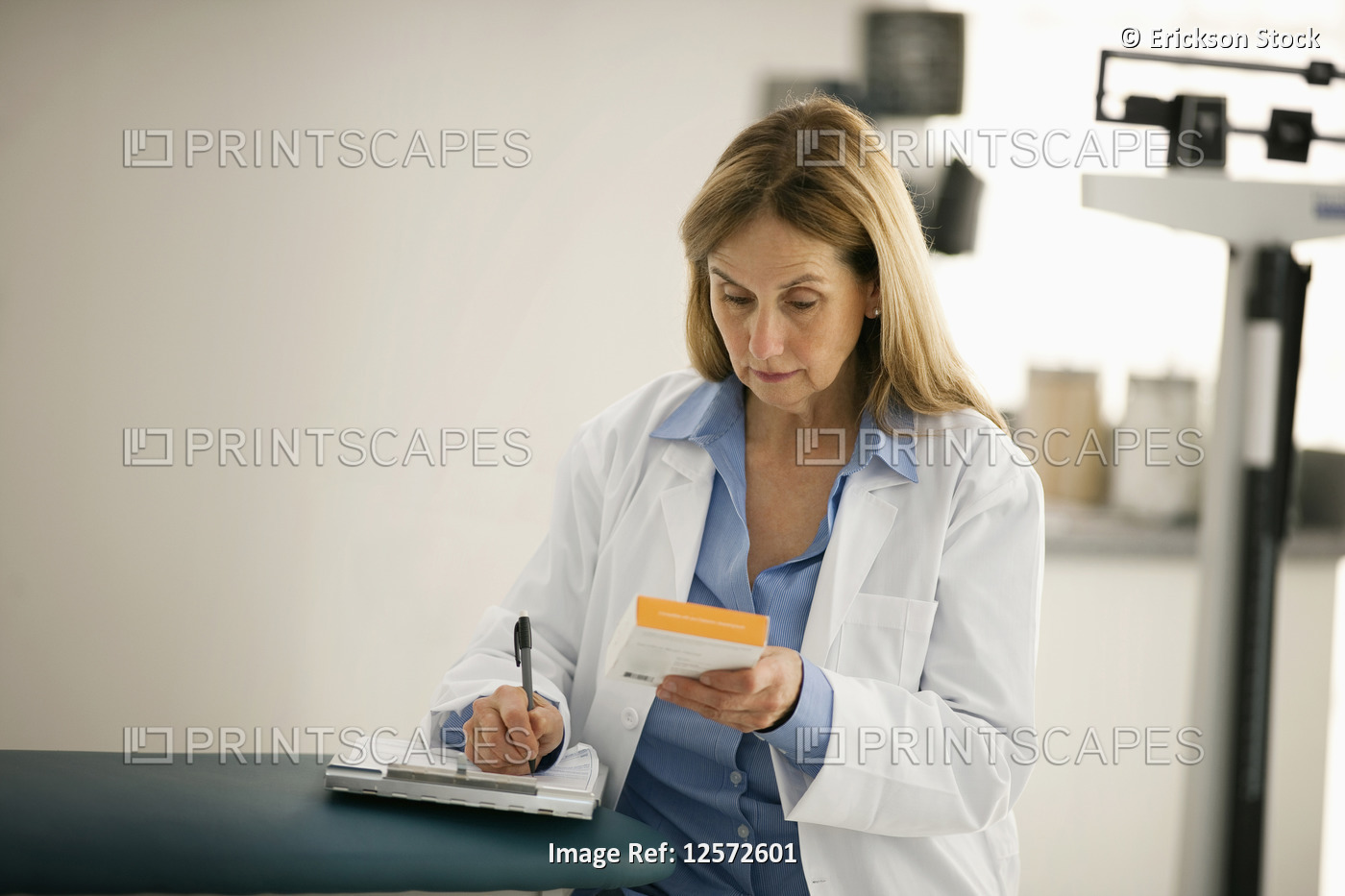 Mid adult doctor taking notes while reading a box of medical supplies