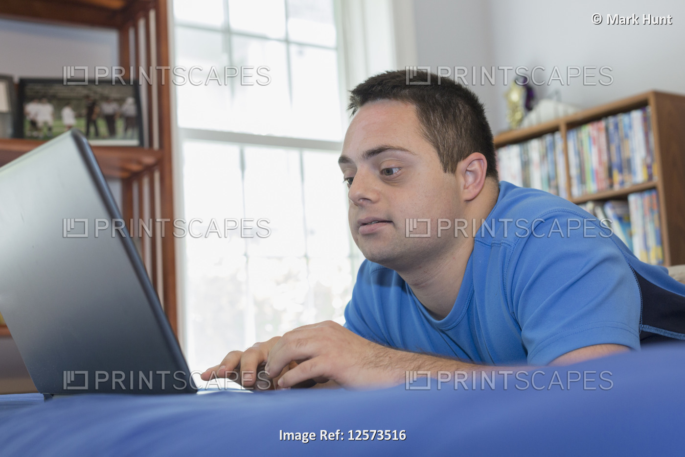 Man with Down Syndrome lying on bed using a laptop