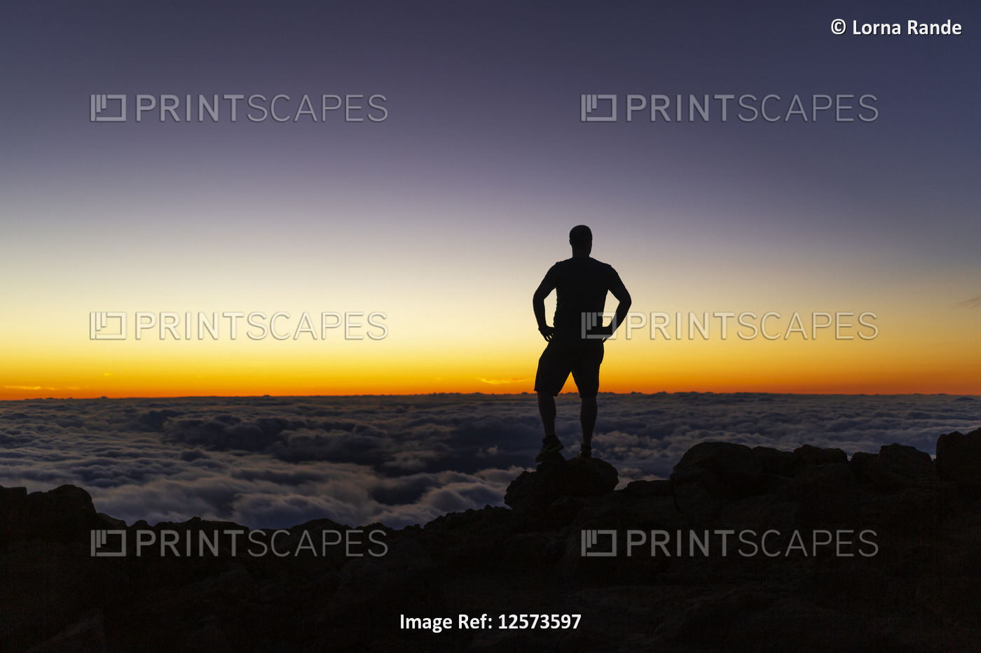 Silhouetted man standing on rock above the clouds at sunset, Haleakala; Maui, ...