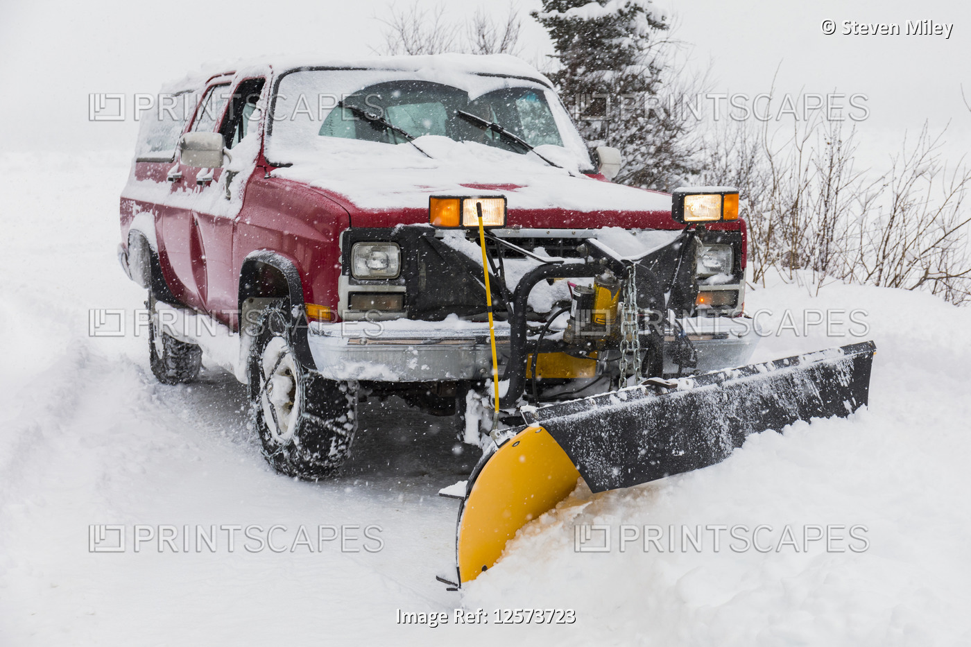 A truck with a plow clears snow from a driveway during blizzard conditions in ...