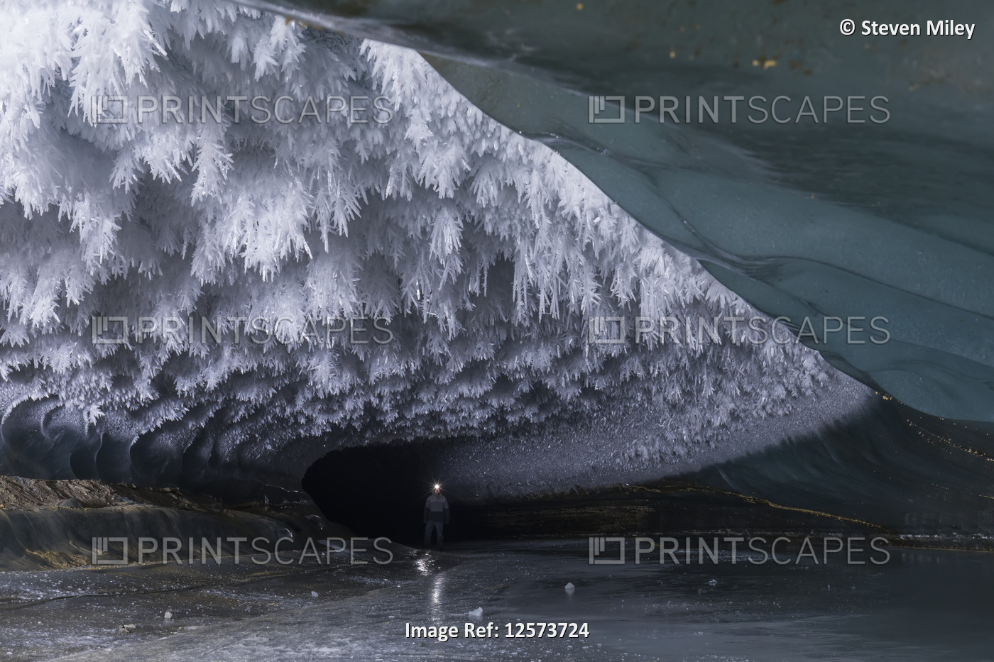 A man with a headlamp explores a Castner Glacier ice cave with hoarfrost ...