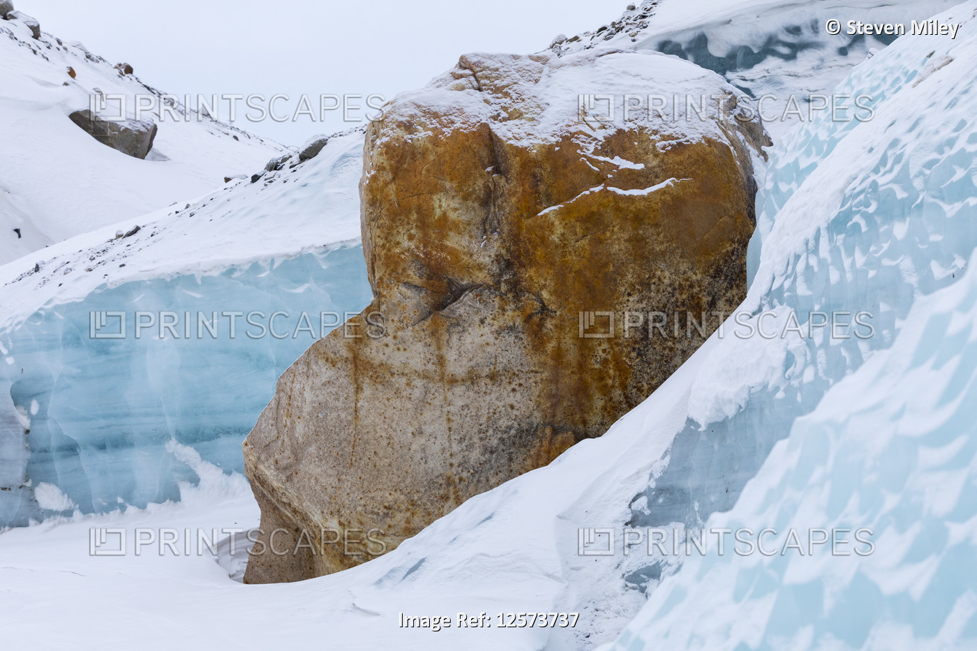 A large boulder leans against the ice of Black Rapids Glacier in winter; ...