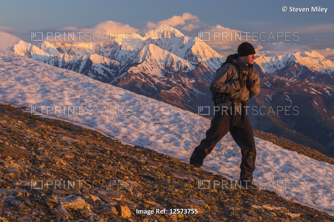 A hiker traverses a mountain slope in the Alaska Range at sunrise; Alaska, ...