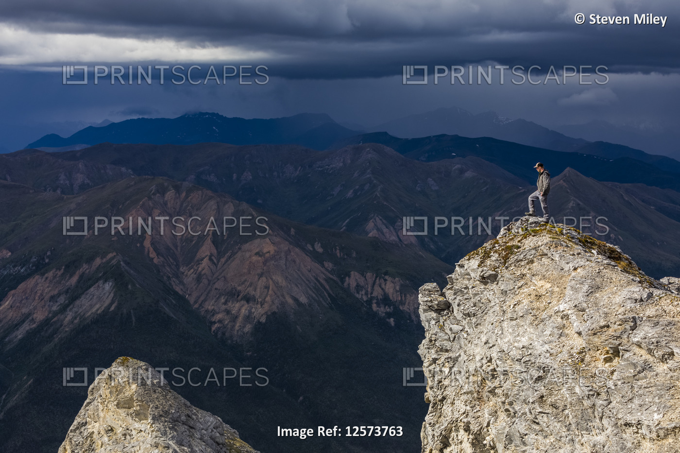 A hiker stands in the sunshine on top of Sukakpak Mountain while storm clouds ...