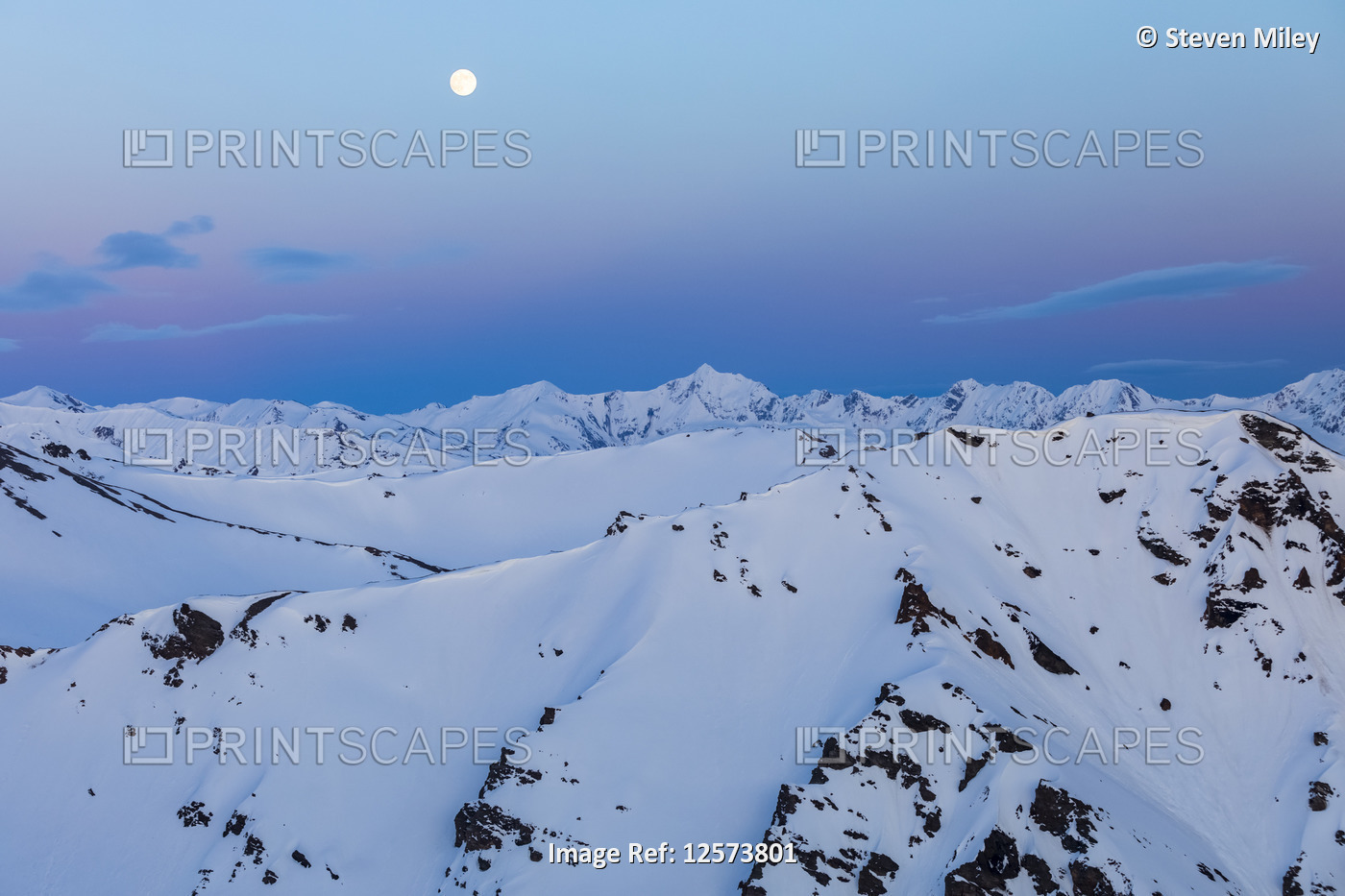 The moon rises over snowy mountain ridges after sunset in the Alaska Range; ...