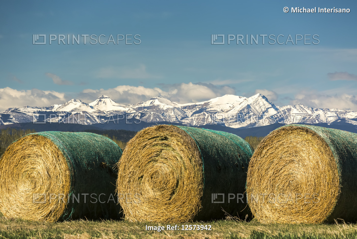 Three large wrapped hay bales with snow-covered mountain range blue sky and ...