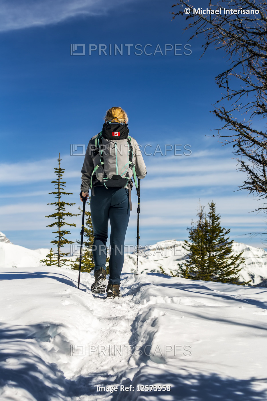 Female hiker on snow-covered pathway with snow-covered mountains, blue sky and ...