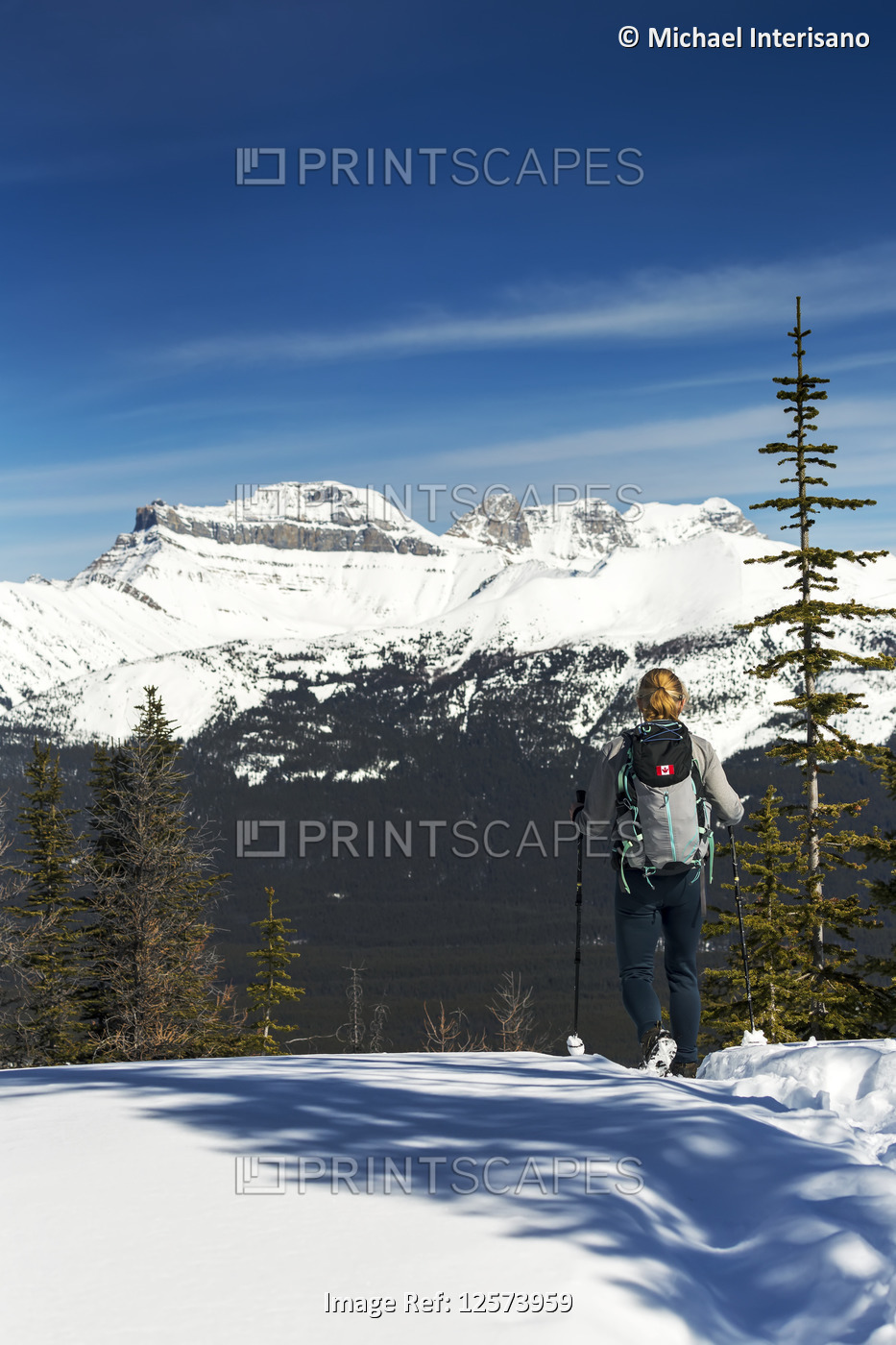 Female hiker on snow-covered pathway with snow-covered mountains, blue sky and ...