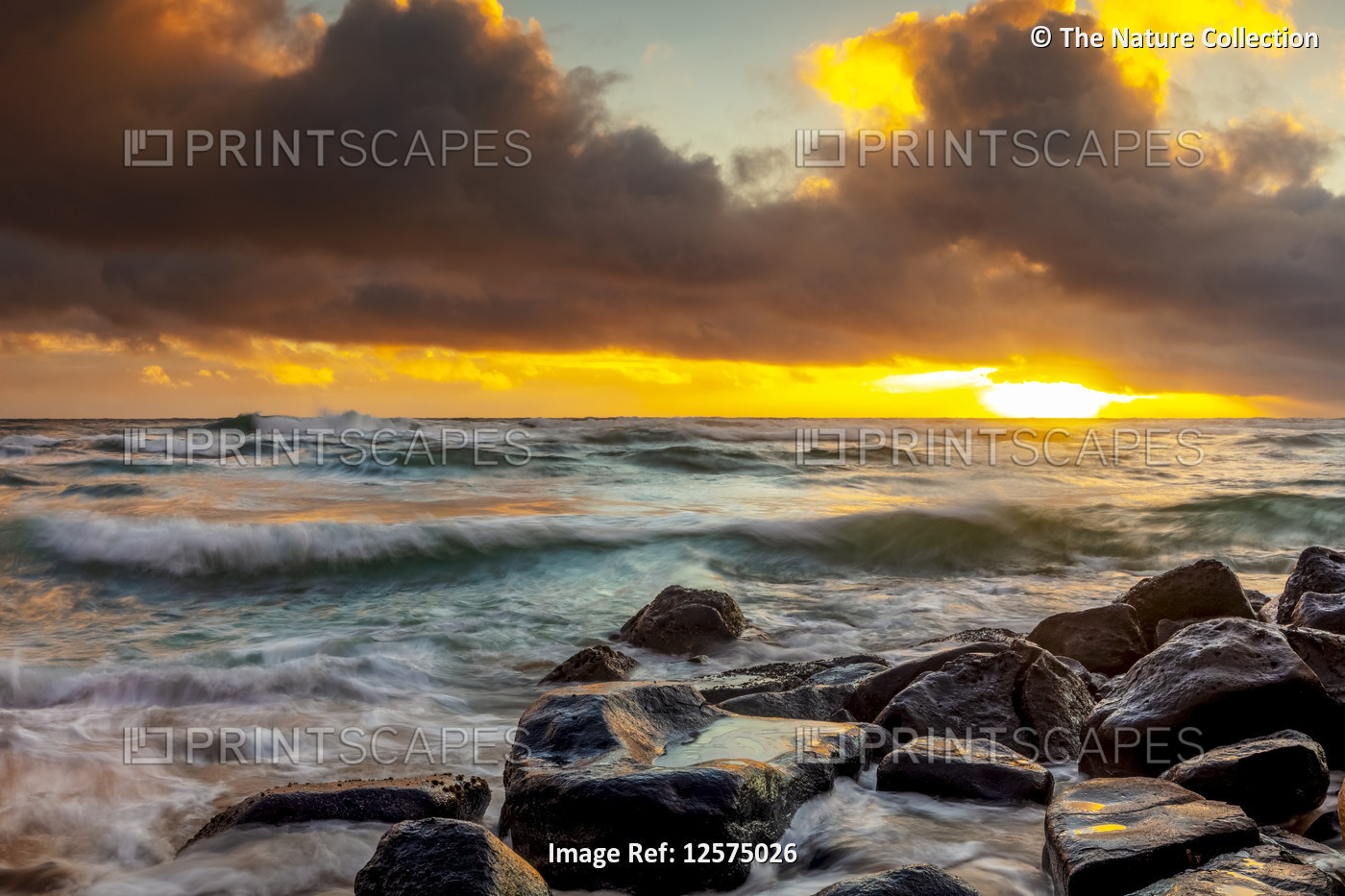 Sunrise over beach and ocean with tide washing up over sand and rocks; Kauai, ...