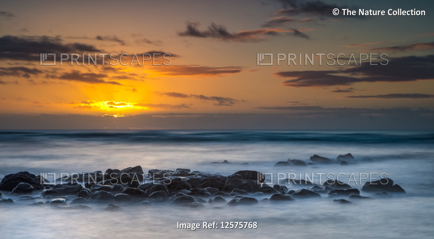 Sunrise over the Pacific Ocean from the rocks on the shore of Kauai; Kauai, ...